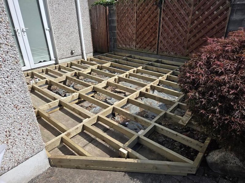 A treated timber deck substructure of joists and noggins laid out over a patio before the boards go down