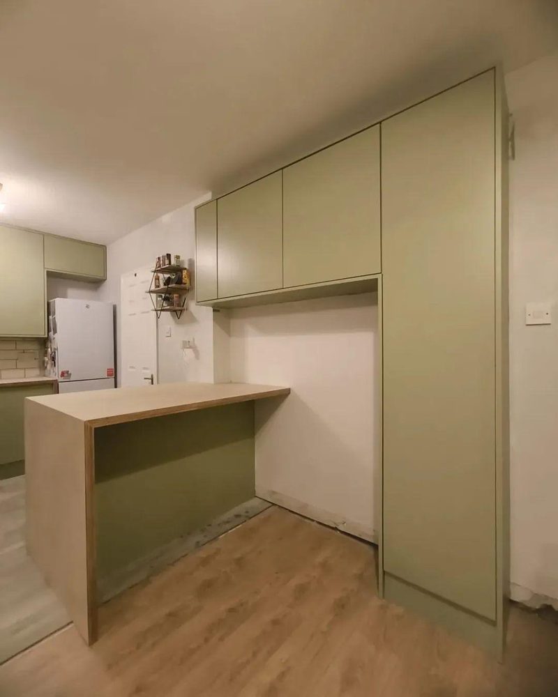 A birch plywood breakfast bar beside full height sage green storage units