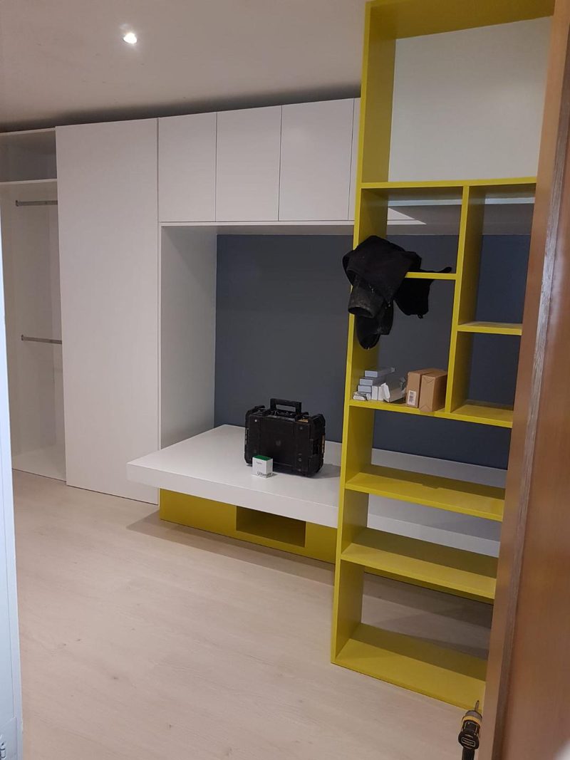 Fitted white wardrobes with a built in desk and a tall yellow open shelving unit