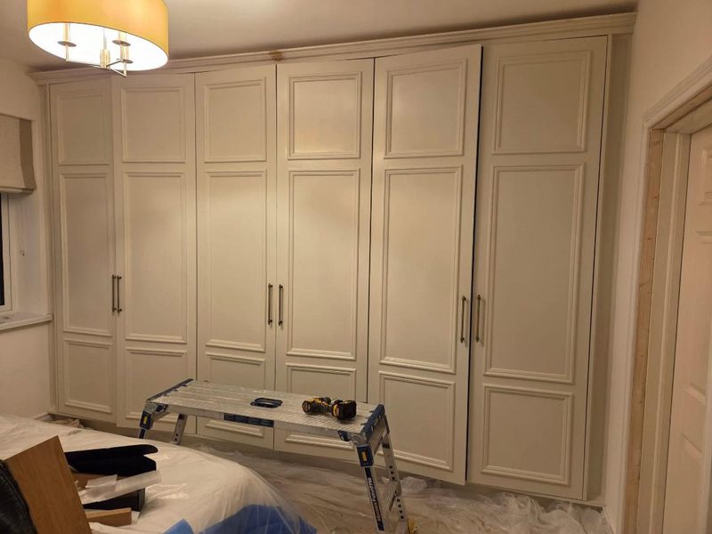 A wall of floor to ceiling fitted wardrobes with panelled doors, painted off white